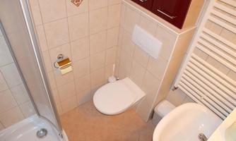 A small bathroom with a shower, a toilet, and a sink. The walls are light tiled, and there is a towel rack.