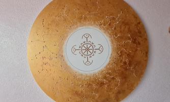 A round wall decoration in shades of gold with a central white area. The pattern inside features a delicate design.