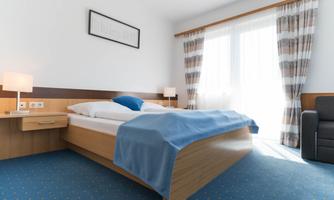 A modern bedroom with a large bed and a blue throw. Large windows let in a lot of light and the decor is simple and elegant.