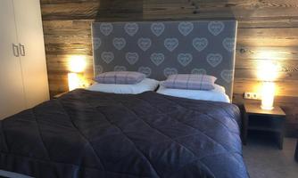 A cozy bedroom with a large double bed and a wooden headboard. The walls are made of wood, and two bedside lamps provide soft light.