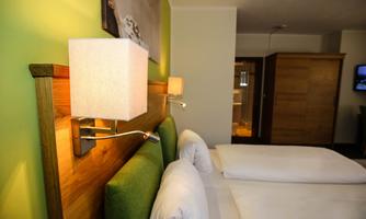 A cozy bedroom with two beds and a modern wooden strip. The walls are painted in a soft green, and there are stylish wall lamps.