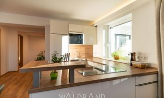 A modern kitchen with bright cabinets and a cooking island. Large windows provide plenty of daylight and a friendly atmosphere.