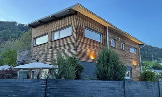 A modern wooden house with large windows and a garden. The facade radiates in the dusk.