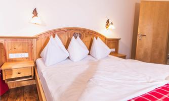 A cozy bedroom with a double bed and large pillows. The wooden furniture and soft lighting create an inviting atmosphere.