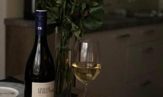 A set dining table with a glass of white wine, a bottle of wine, and a vase with red roses. In the background, a modern kitchen can be seen.