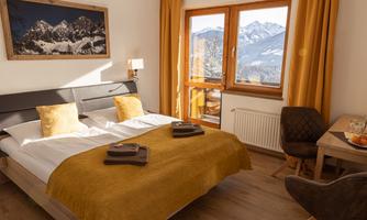 A cozy room with a double bed and golden cushions. An impressive mountain landscape can be seen through the window.