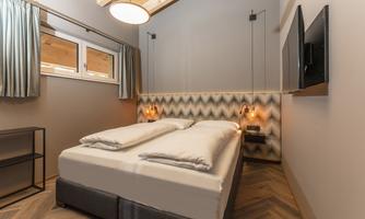 A modern bedroom with a large double bed and subtle walls. There is a TV and windows with curtains that provide pleasant light.