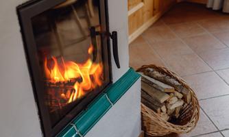 A cozy wood stove with a blazing fire. Next to it stands a basket of firewood.