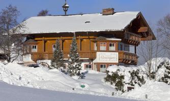A charming wooden house in the snow with a large balcony. The surrounding landscape is wintry and picturesque.