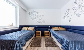 A modern bedroom with two single beds and elegant bedding. The walls are decorated with stylish patterns and there is plenty of natural light coming through the window.