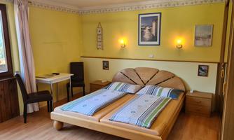 A cozy bedroom with a large double bed and a bright yellow wall color. A table and chair are in the corner, complemented by a city view on the wall.