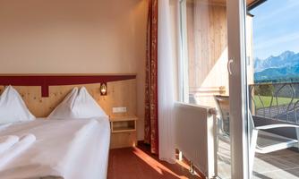 A cozy room with two beds and a balcony. The view shows the mountains and plenty of daylight.