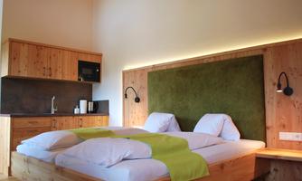 A modern bedroom with a double bed and wooden paneling. The cozy atmosphere is enhanced by a green wall and soft lighting.