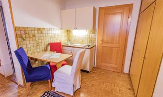 Small kitchen with a dining table and two chairs. Bright walls and a wooden cabinet create a cozy atmosphere.