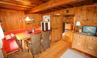 A cozy room with wooden walls and a dining table. On the left side, there is a bench and on the right, a cabinet.