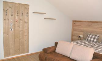 A cozy room with a wooden bed and a beige couch. Some hooks are hanging on the wall and there are shelves for decoration.