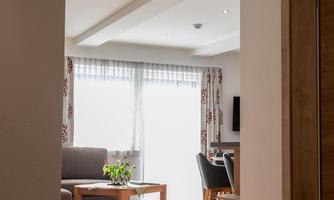 A bright living area with a cozy sofa and a table. Sunshine streams through large windows, creating an inviting atmosphere.