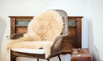 A cozy chair with a soft fur and a rustic wooden backrest. Next to the chair is an old suitcase.