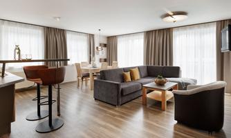 A modern living room with a cozy seating area and a dining table. Large windows allow for bright light and an inviting atmosphere.