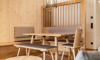 A cozy dining area made of wood with a table and benches. The walls are lined with light wood, creating a warm atmosphere.