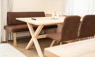A modern dining area with a wooden table and a bench. The furniture is simple and in warm colors.