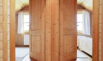 A wooden room with a double door in the middle. Bright windows let in plenty of daylight and give the atmosphere a cozy mood.