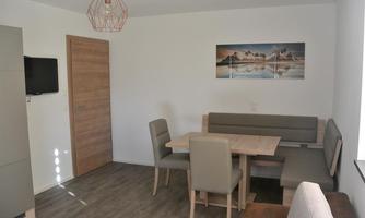 A modern dining room with a table and seating. A picture of a mountain landscape hangs on the wall.