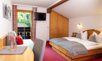 A cozy room with a double bed and a table. Large windows offer a view of the surroundings, and the room has rustic wooden paneling.