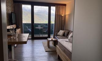 A modern room with a cozy sofa and a dining table. Large windows provide a view of the nature outside.