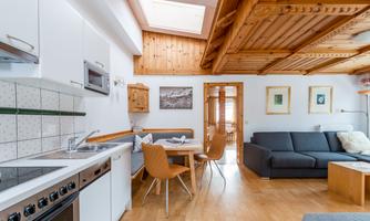 A modern living kitchen with a wooden ceiling and bright walls. The room is cozy furnished with a dining table and a comfortable sofa.
