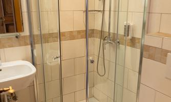 A modern bathroom with a glass walk-in shower and a sink. The walls are tiled, and the floor has a light color.