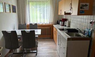 A modern kitchen with wood-colored cabinets and a table with four chairs. The window lets in plenty of daylight and offers a view outside.