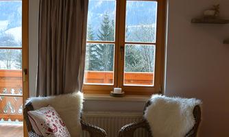 A cozy room with two wicker armchairs and a window that offers a view of the mountains. The windows let in plenty of daylight, and the decor feels warm and inviting.