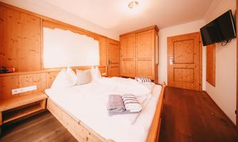 A cozy bedroom with wooden furniture and a large bed. A television is hanging on the wall, and there are fresh towels on the bed.