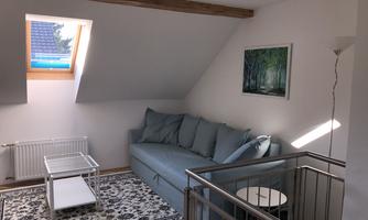 A cozy living space with a blue couch and a decorative rug. A small table and a window provide plenty of daylight.