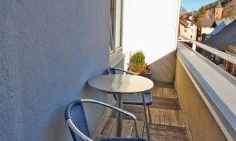 A small balcony with two chairs and a table. The scenery shows a bright blue sky and a peaceful environment.