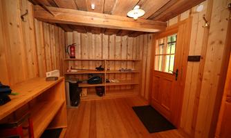 A cozy room with wooden walls and a wooden floor. There are shelves and an entrance door that lets in plenty of daylight.