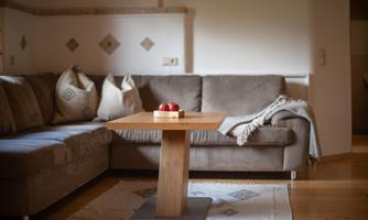 A cozy living room with a gray couch and decorative cushions. On a wooden tray, three apples lie on a table.
