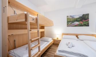 A modern room with a bunk bed and a double bed.  
A landscape painting hangs on the wall, conveying a calm and cozy impression.