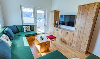 A modern living room with a green couch and a wooden table. Large windows provide plenty of light and a welcoming atmosphere.