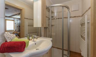 A modern bathroom with a shower, a sink, and bright tiles. Towels in red and green are neatly laid out on the sink.