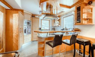 A modern kitchen with wooden details and elegant bar stools. Large windows provide plenty of natural light.