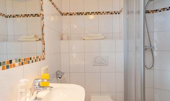 A modern bathroom with a shower, sink, and toilet. The walls are adorned with light tiles, complemented by colorful accent tiles.