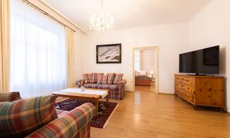 A bright living room with checkered sofas and a cozy wooden table. In the background, there is a television and a beautiful cabinet.