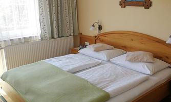 A cozy bedroom with a double bed and fresh bedding. Large windows provide bright light and an inviting atmosphere.