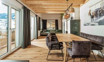 A modern dining room with a large wooden table and comfortable armchairs.  
Large windows let in plenty of light and offer a view of the mountains.