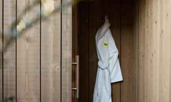 A wellness area with wooden paneling. A white bathrobe hangs on the wall, next to it are slippers.