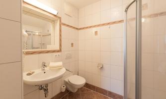 A modern bathroom with bright tiles and a round sink. There is a shower, a toilet, and a mirror above the sink.