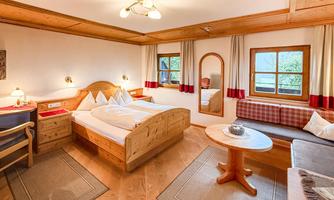 A cozy bedroom with a wooden double bed. The walls are light-colored, and there are large windows with a nice view outside.