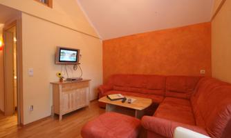 A cozy living room with a red couch and a wooden table. A TV hangs on the wall and the walls are painted in warm tones.